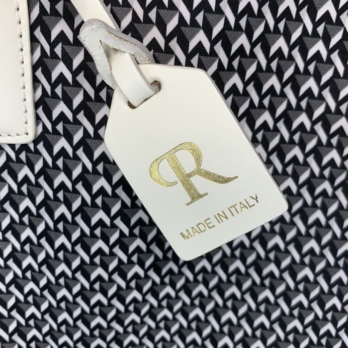 На тлі чорно-білої геометричної тканини звисає біла шкіряна бирка ROBERTA PIERI з літерами «R» золотого кольору та написом «MADE IN ITALY».