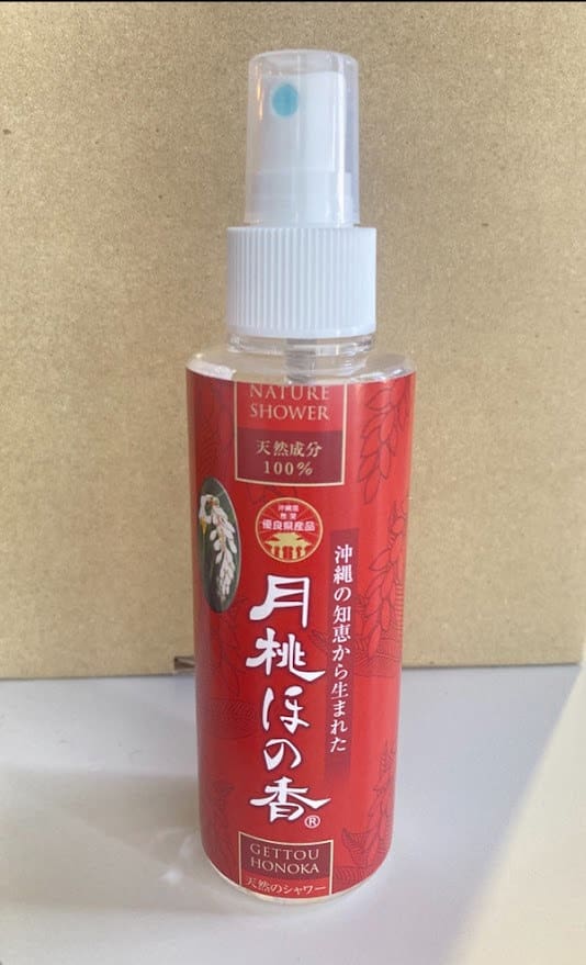 Червона пляшка з пульверизатором з написом «Nature Shower» на бежевому тлі. Біла розпилювальна насадка і ковпачок.